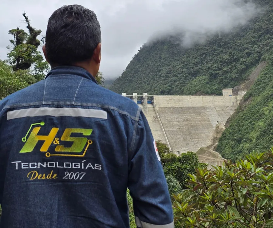 Técnico de H&S, de espaldas, observando una represa entre montañas cubiertas de selva